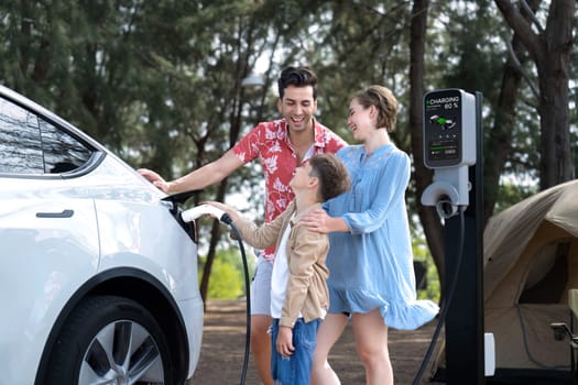 Outdoor adventure and family vacation camping in nature travel by eco friendly car for sustainable future. Lovely family recharge EV car with EV charging station in campsite. Perpetual