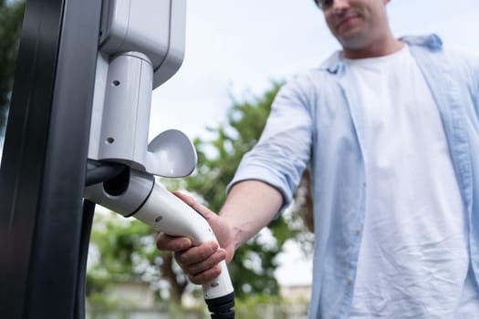 Eco-friendly conscious man recharging modern electric vehicle from EV charging station. EV car technology utilized as alternative transportation for future sustainability. Synchronos