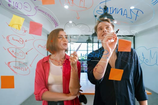 Couple of young creative start up business people brainstorming idea and solving problems by using sticky note and mind map at glass board, meeting room. discussing, working together. Immaculate.