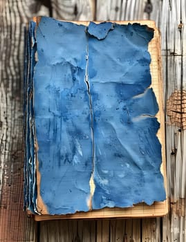 An art book with azure pages rests on a wooden table, its textile sleeve in electric blue contrasting with the grey rectangle of the wood