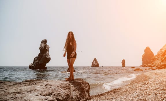 Woman travel sea. Young Happy woman in a long red dress posing on a beach near the sea on background of volcanic rocks, like in Iceland, sharing travel adventure journey