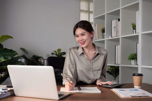 Young Asian business woman sitting in the office using a calculator to calculate business numbers..