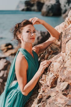 Woman green dress sea. Woman in a long mint dress posing on a beach with rocks on sunny day. Girl on the nature on blue sky background