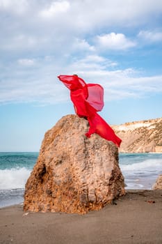 woman sea red dress. Woman with long hair on a sunny seashore in a red flowing dress, back view, silk fabric waving in the wind. Against the backdrop of the blue sky and mountains on the seashore