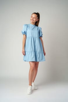 Young happy smiling woman in a light blue dress on a gray background close up