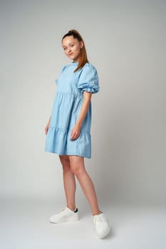 Young happy smiling woman in a light blue dress on a gray background close up