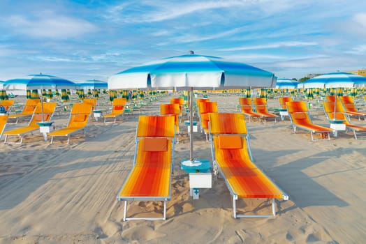Blue umbrellas and chaise lounges on the beach of Rimini in Italy.