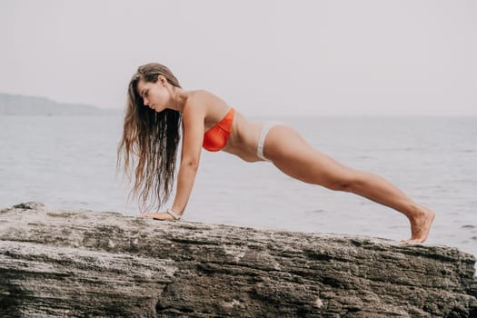 Woman meditating in yoga pose silhouette at the ocean, beach and rock mountains. Motivation and inspirational fit and exercising. Healthy lifestyle outdoors in nature, fitness concept.