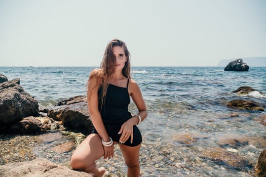 Woman travel sea. Young Happy woman in a long red dress posing on a beach near the sea on background of volcanic rocks, like in Iceland, sharing travel adventure journey