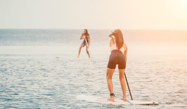 Sea woman and man on sup. Silhouette of happy young woman and man, surfing on SUP board, confident paddling through water surface. Idyllic sunset. Active lifestyle at sea or river