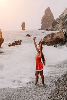 Woman travel sea. Young Happy woman in a long red dress posing on a beach near the sea on background of volcanic rocks, like in Iceland, sharing travel adventure journey