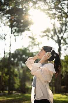 Pleased young woman listening the music with headphone and breathing fresh air in the park.