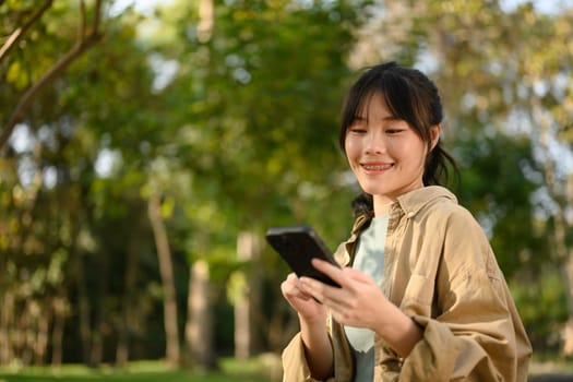 Attractive young woman sitting on bench in park and texting on her mobile phone.