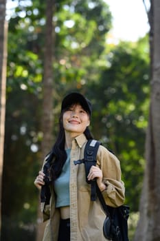 Portrait of female tourist with backpack walking and breathing fresh air in the forest.