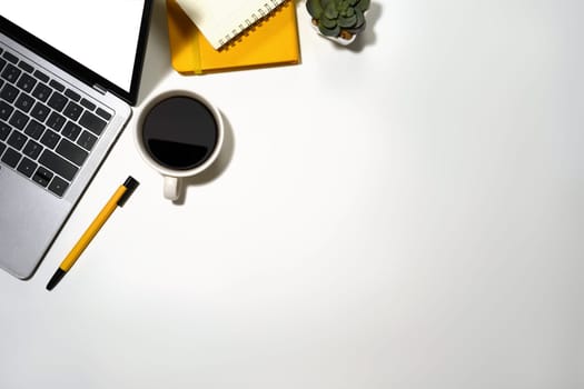 A cup of coffee, laptop computer and notepad on white office desk.