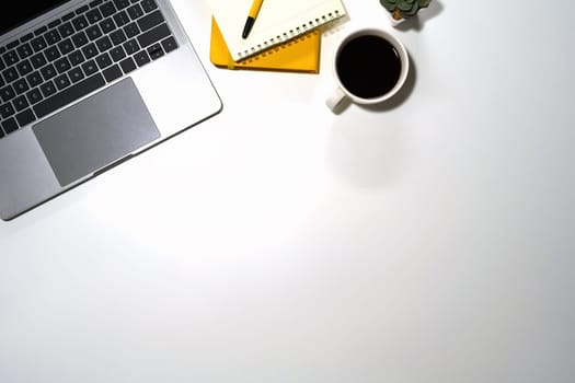 Laptop computer, notepad and coffee mug on white office desk. Top view with copy space.