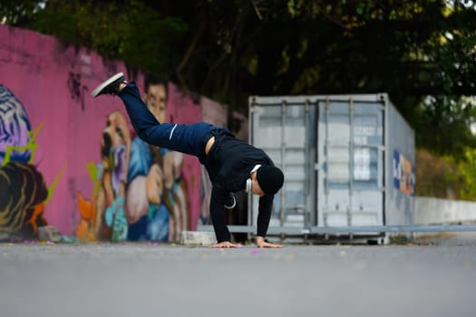 Young Asian male hip hop dancer practicing dance, performing freestyle moves in the city street.