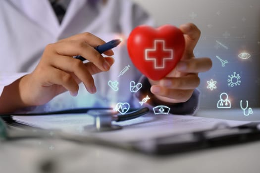 Closeup cardiologist holding red heart shape with virtual medical icons. Health care concept.