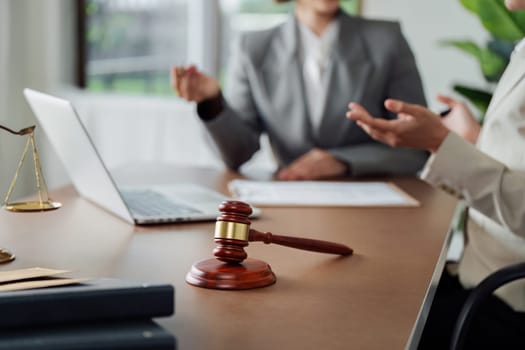 Two women are sitting at a desk with a laptop and a gavel. They are discussing something important