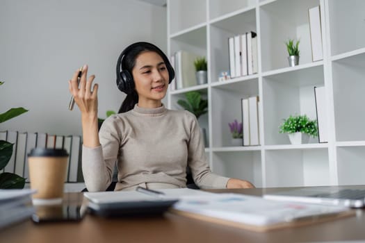 A woman wearing headphones is sitting at a desk with a laptop and a cup of coffee. She is smiling and she is enjoying her work