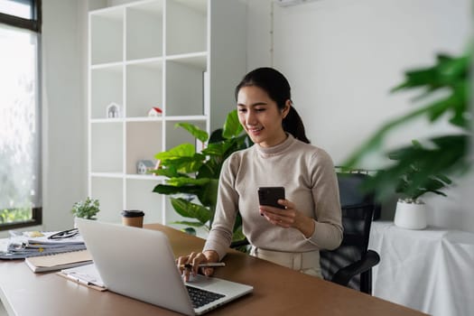 business woman using smartphone while working on laptop, synchronize data between computer and gadget in office, use corporate devices and business application.