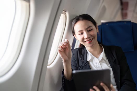 Smiling happy business woman asian flying and working in an airplane in first class, Woman sitting inside an airplane using digital tablet.