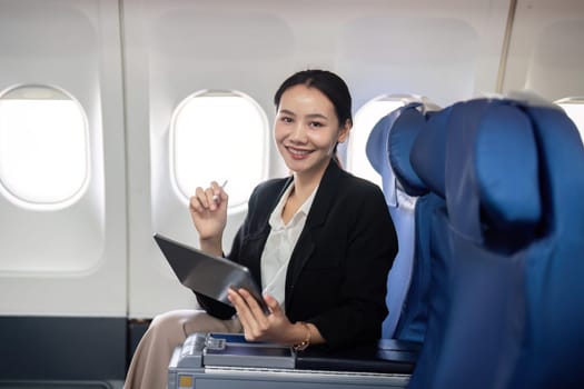 Smiling happy business woman asian flying and working in an airplane in first class, Woman sitting inside an airplane using digital tablet.