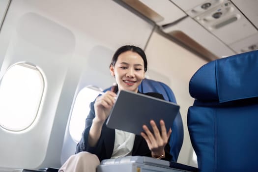 Smiling happy business woman asian flying and working in an airplane in first class, Woman sitting inside an airplane using digital tablet.