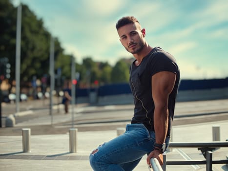 A man is seated on the metal bench, looking out into the distance. He appears relaxed and thoughtful as he takes in the surroundings.