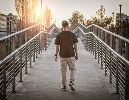 A man is walking across a bridge that spans over a street. The man appears to be in motion, with the traffic flowing beneath him.