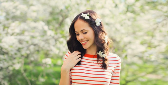 Portrait of lovely happy smiling young woman in spring blooming garden with white flowers on the trees in park