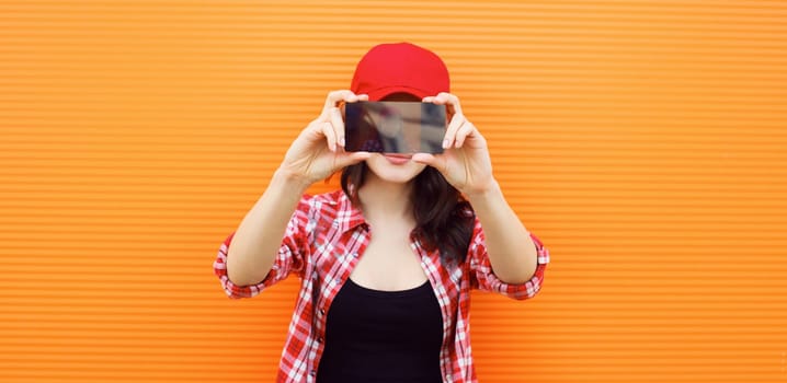 Summer portrait of happy cheerful young woman taking selfie with mobile phone on colorful orange background on city street