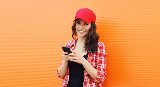 Portrait of happy smiling young woman with mobile phone in summer red baseball cap on colorful orange background