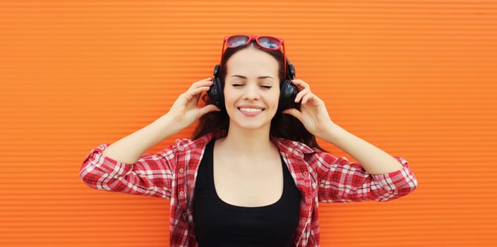 Summer portrait of happy smiling young woman listening to music in headphones on colorful orange background