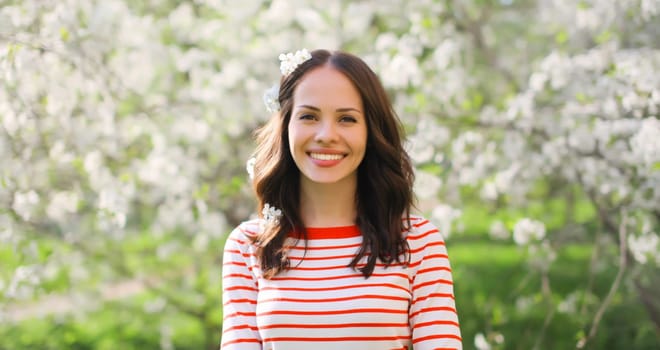 Portrait of lovely happy smiling young woman in spring blooming garden with white flowers on the trees in park