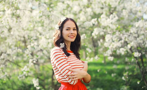 Portrait of lovely happy smiling young woman in spring blooming garden with white flowers on the trees in park