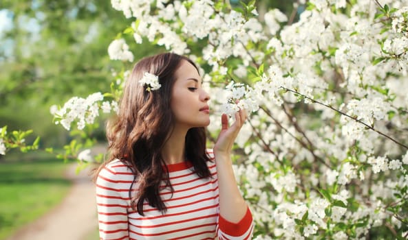 Portrait of lovely happy smiling young woman in spring blooming garden with white flowers on the trees in park