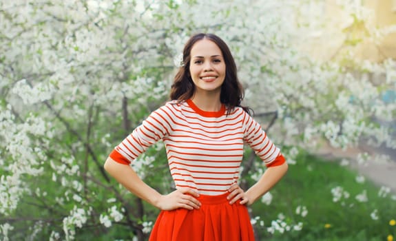 Portrait of lovely happy smiling young woman in spring blooming garden with white flowers on the trees in park