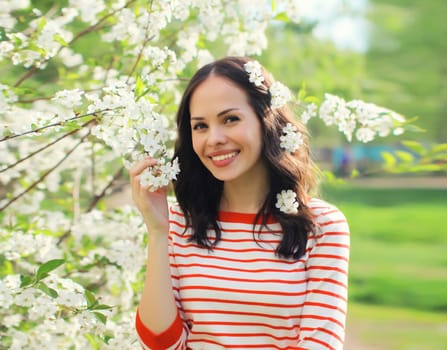 Portrait of lovely happy smiling young woman in spring blooming garden with white flowers on the trees in park