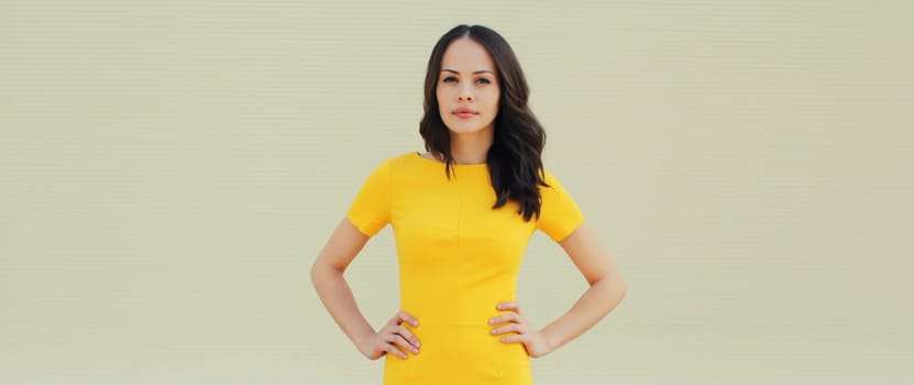 Portrait of beautiful young brunette woman model posing in yellow dress on city street