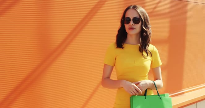 Portrait of stylish beautiful young woman posing with shopping bags on orange background in city