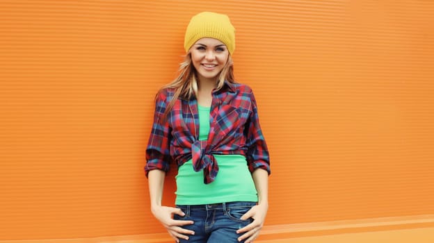 Beautiful happy smiling young blonde woman posing in casual clothes, yellow hat on colorful orange background in the city