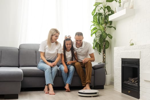 Family resting while robotic vacuum cleaner doing its work at home.