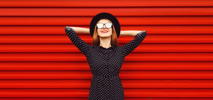 Portrait of beautiful smiling young woman wearing black round hat on red background