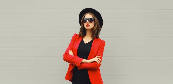 Stylish elegant woman posing in business suit, red blazer jacket and black round hat