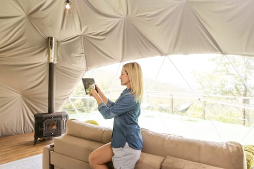 woman holding a tablet with the smart home application in a glamping dome tent domestic.