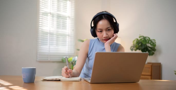 Asian college student who is bored Sitting in front of a laptop studying online through a video calling program on a laptop at home..