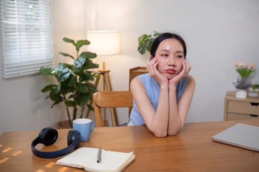 Asian college student who is bored Sitting in front of a laptop studying online through a video calling program on a laptop at home..