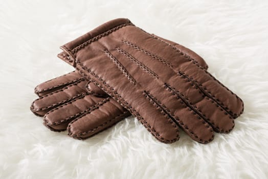 Pair of men's brown leather gloves with accent stitching in dark brown over white fur.