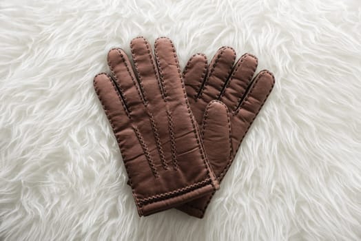 Pair of men's brown leather gloves with accent stitching in dark brown over white fur.